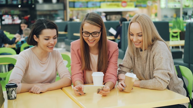 Three friends looking at a phone at a table.