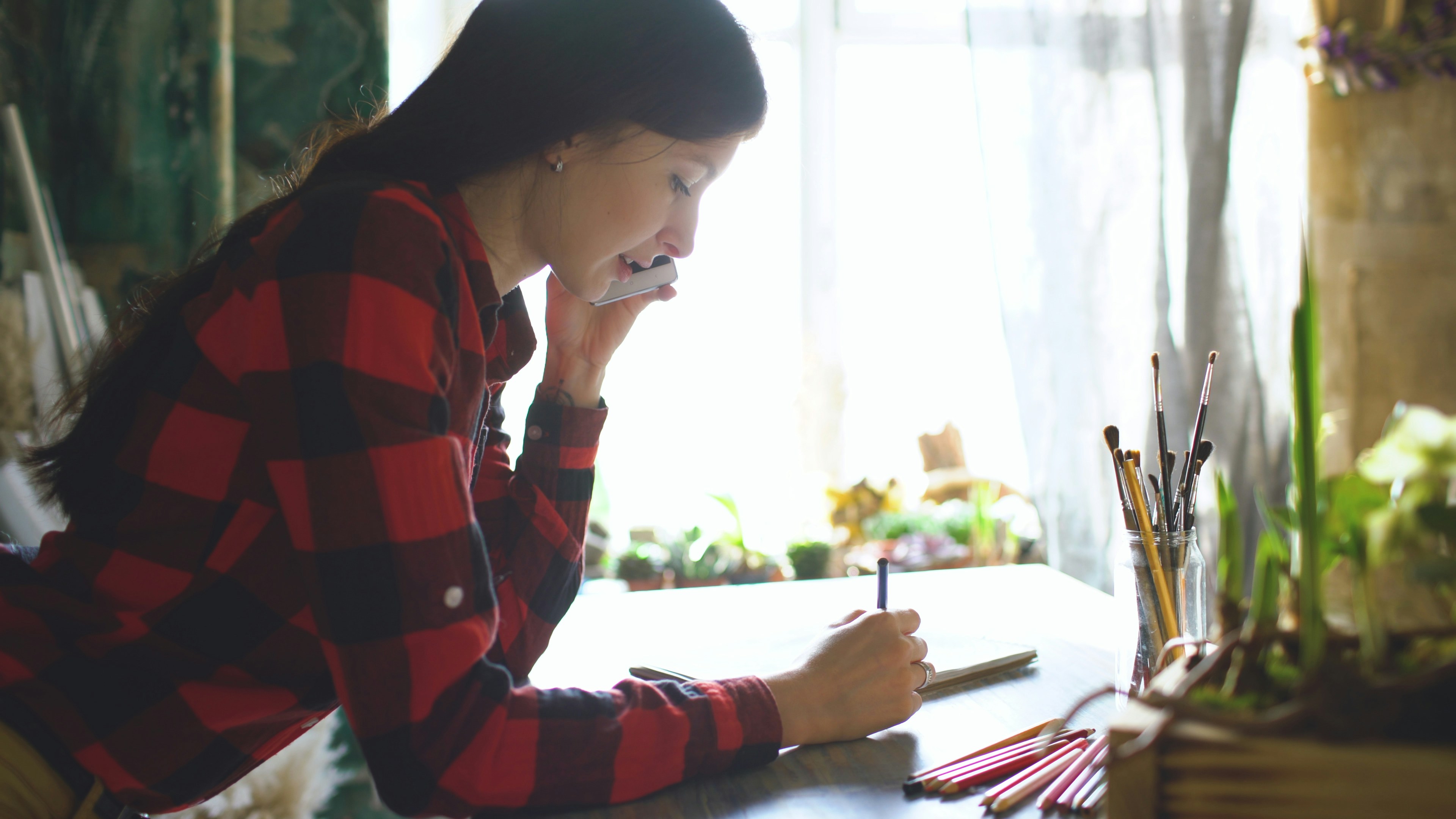 Young woman on phone, sketching in notebook.