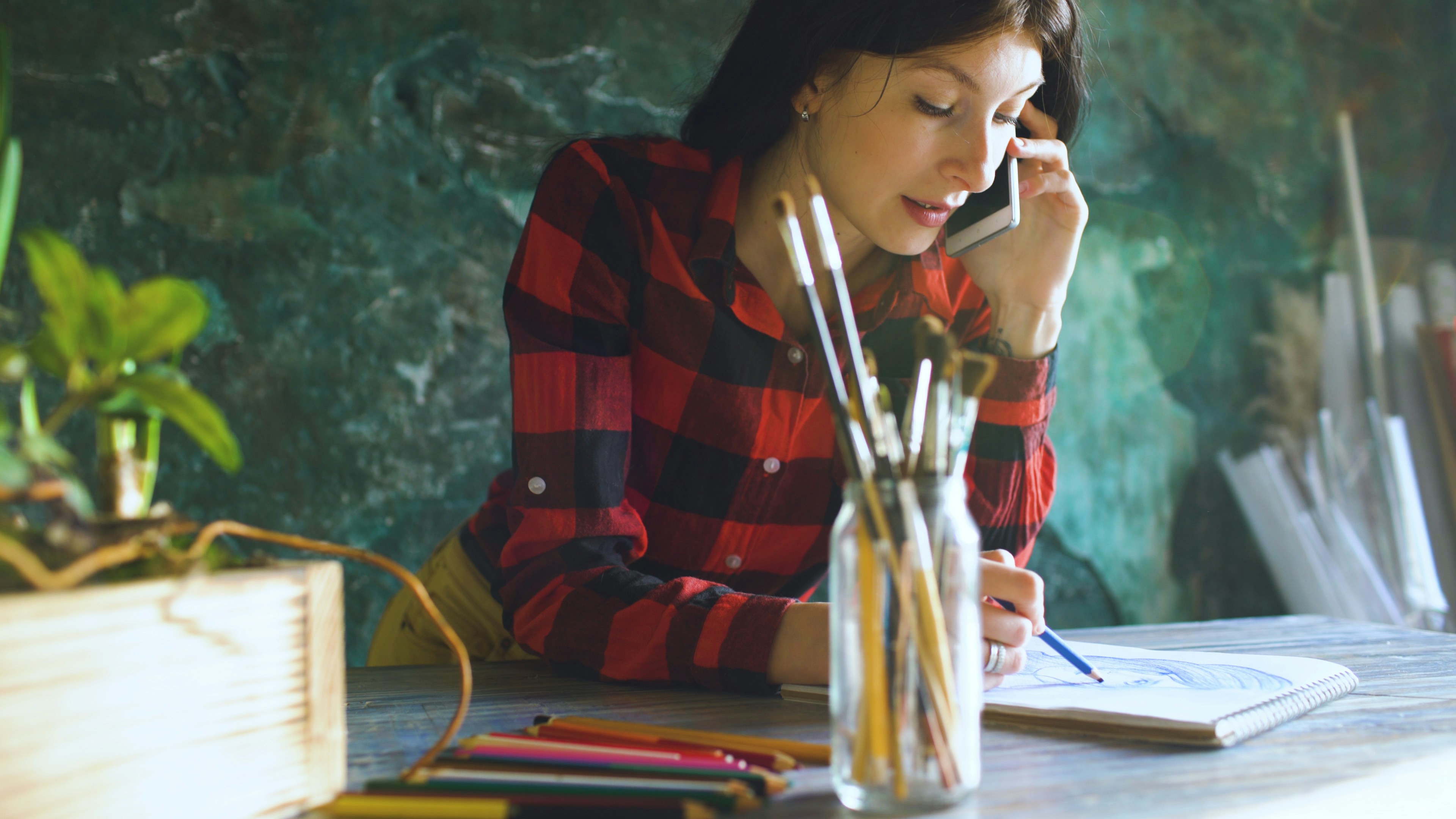Woman talking on phone while sketching at desk.