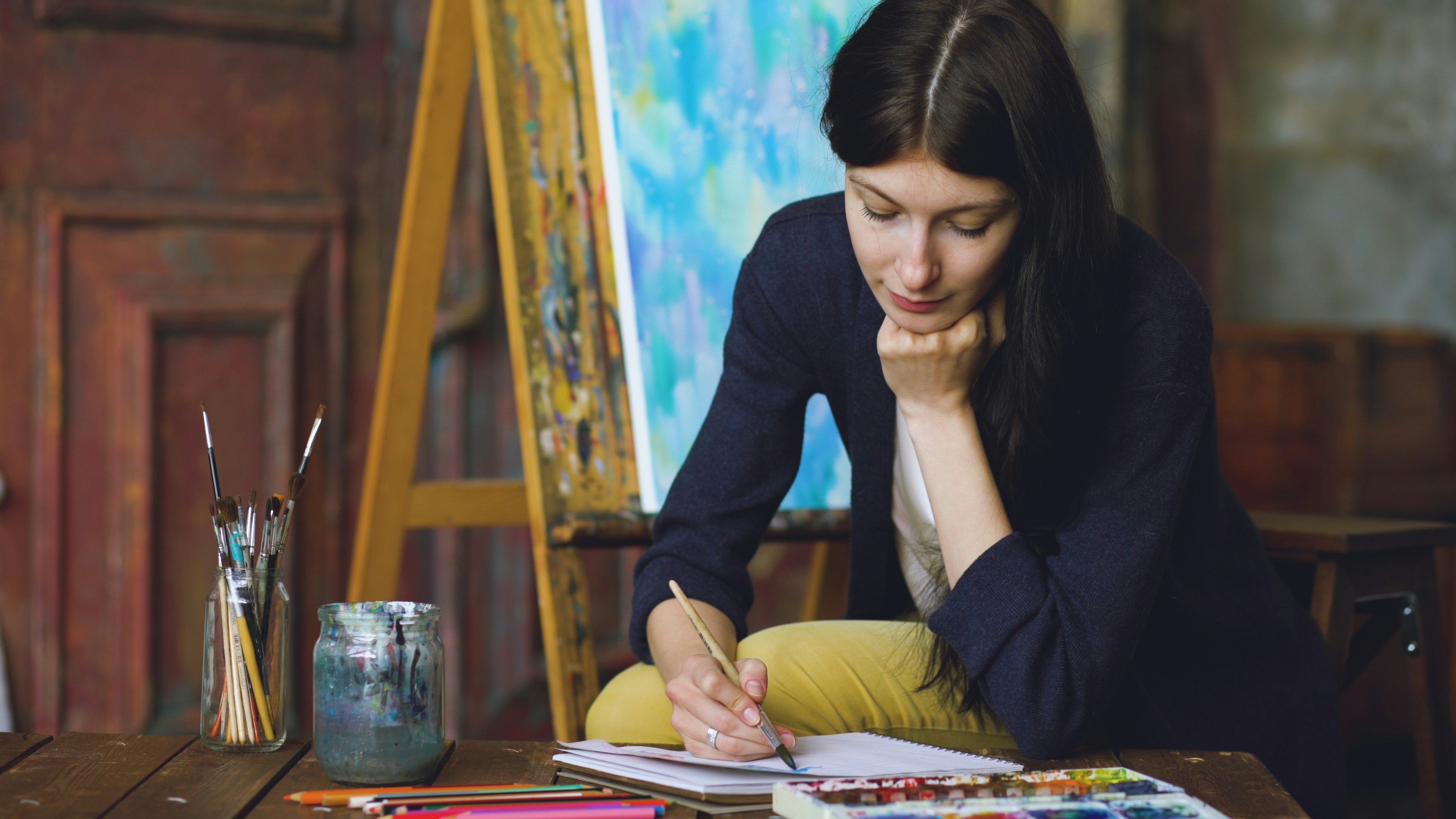 Art student standing alone in a studio space before graduation, surrounded by unfinished works, sketchbooks, natural light, suggesting artistic transition, and a life beginning beyond school.