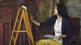 A woman painting on an easel in a studio.
