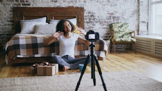 Woman waves at camera in bedroom with tripod