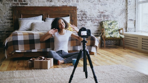 Woman waves at camera in bedroom with tripod