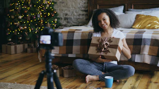 Woman holding a gift in front of a christmas tree.