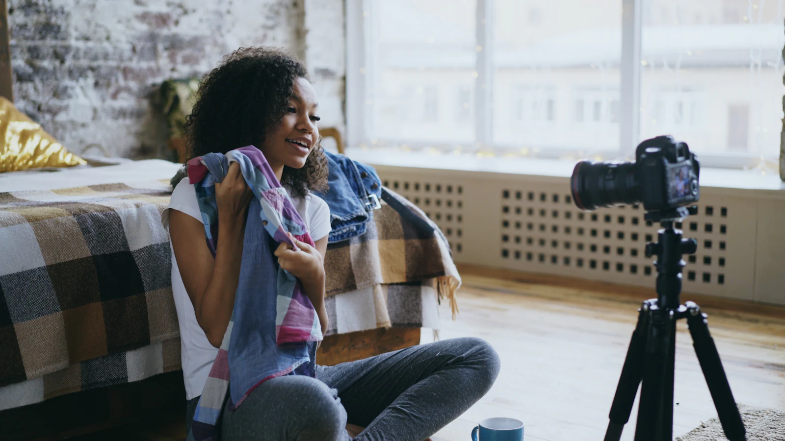 A creator holding up a shirt to a camera on a tripod while filming a clothing review at home
