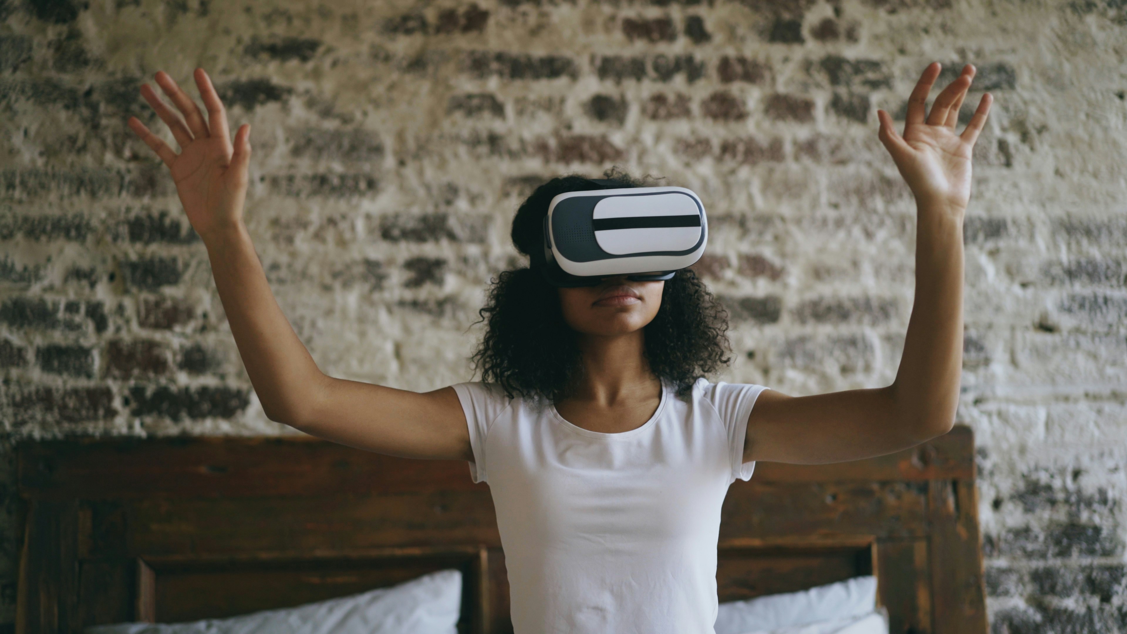 Curly african american woman getting experience using VR 360 headset glasses of virtual reality sitting in bed and moving hands at home