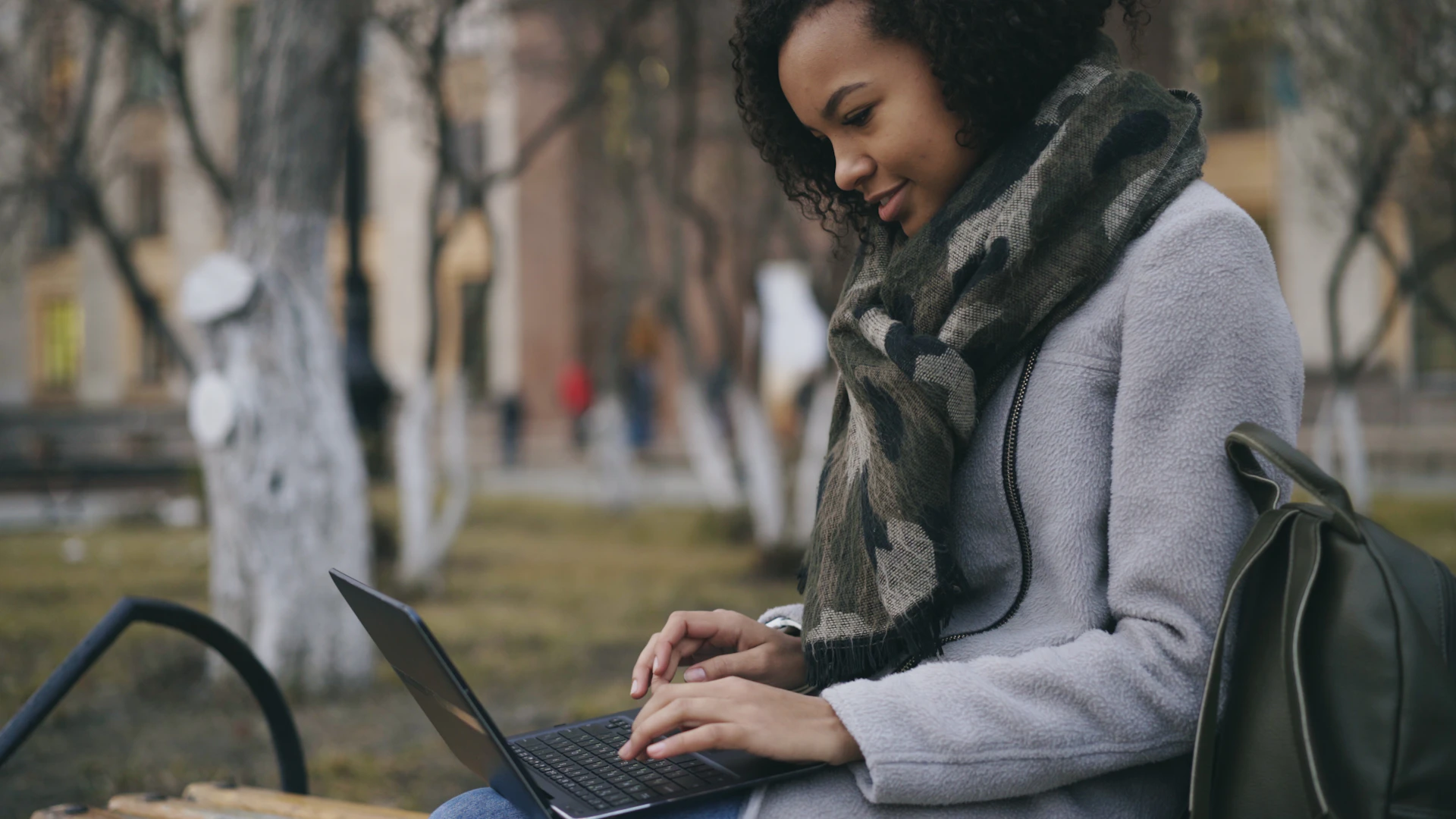 Young woman typing on a laptop outdoors on a bench.