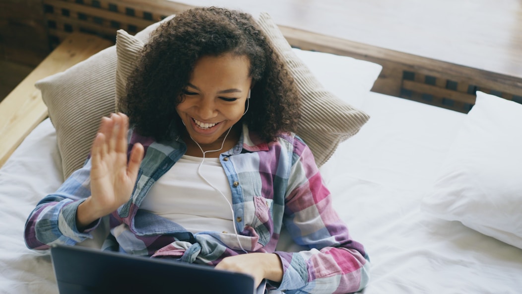 Young woman waving hello while video chatting on laptop.