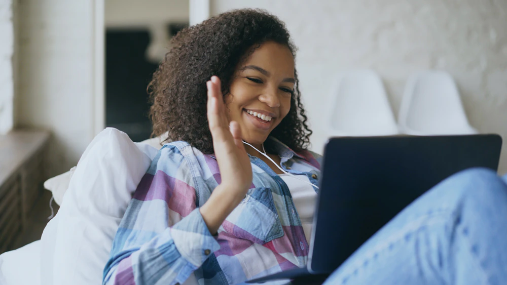A smiling patient waving hello during a video call from her couch at home