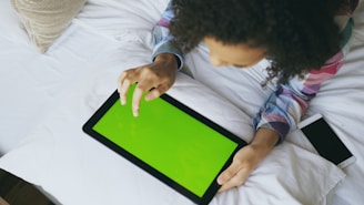 Young person using a tablet with a green screen.