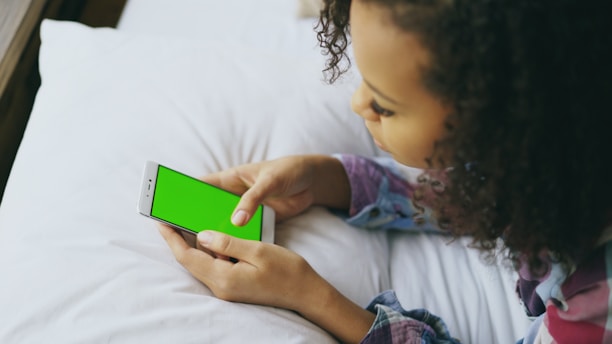 Young girl holding a smartphone with a green screen.