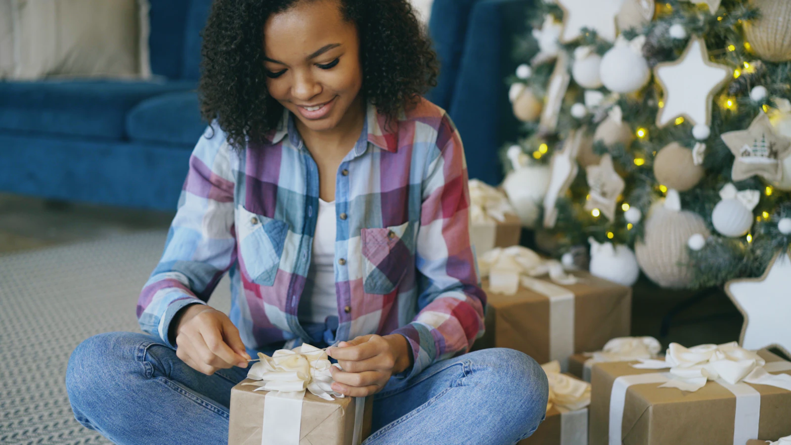 Woman wrapping Christmas gifts at home near a decorated tree