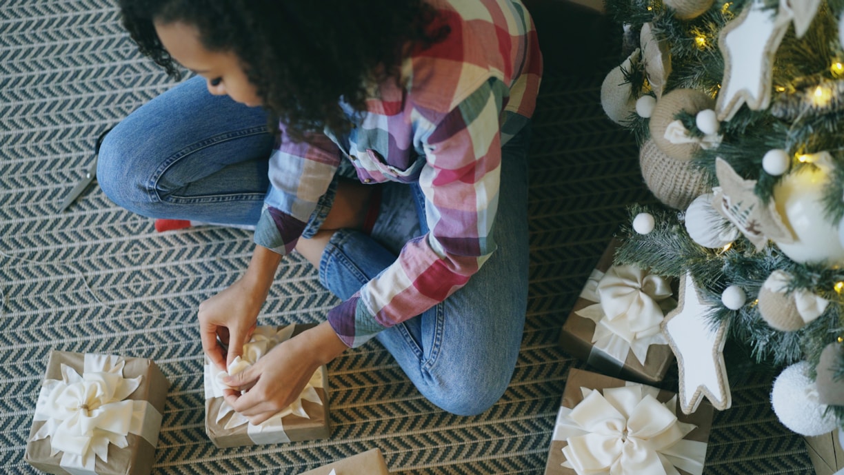 Woman wrapping gifts by a decorated christmas tree