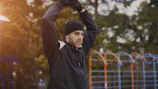Man in black hat stretching outdoors with arms raised outdoors.