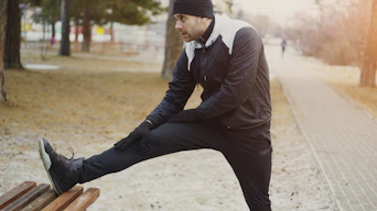 Man stretching leg on park bench during cold weather