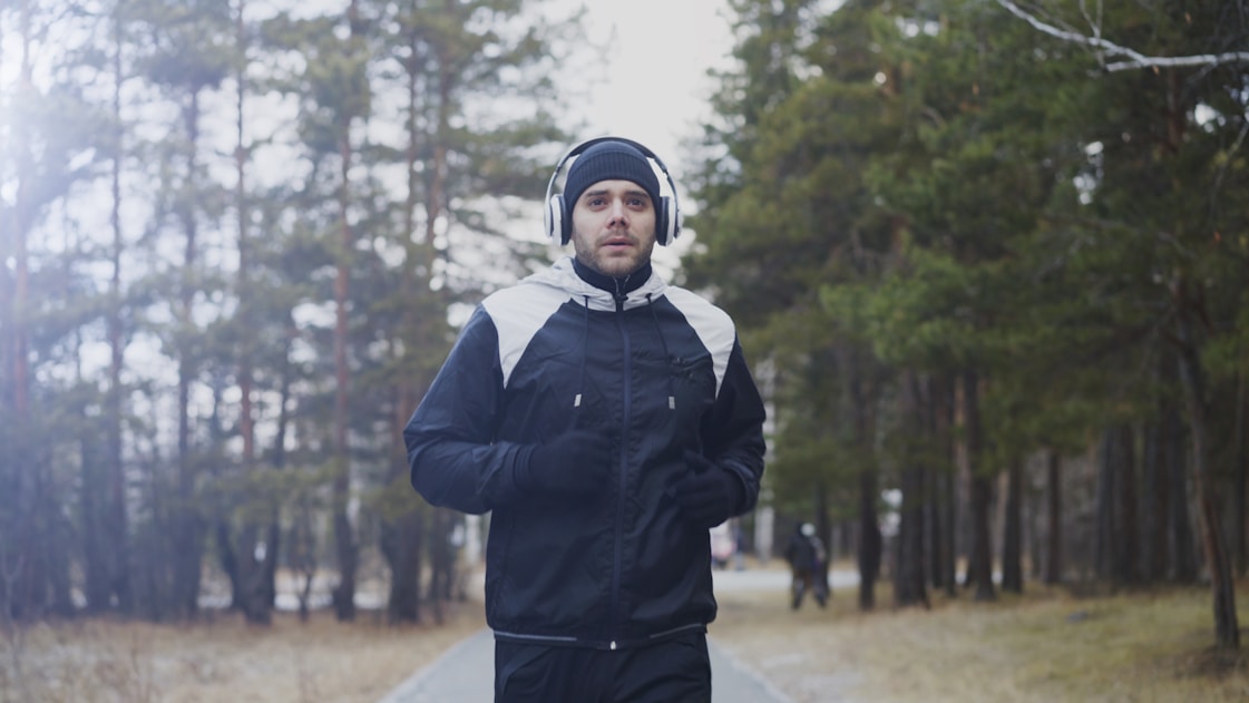 Man running in a forest with headphones on.