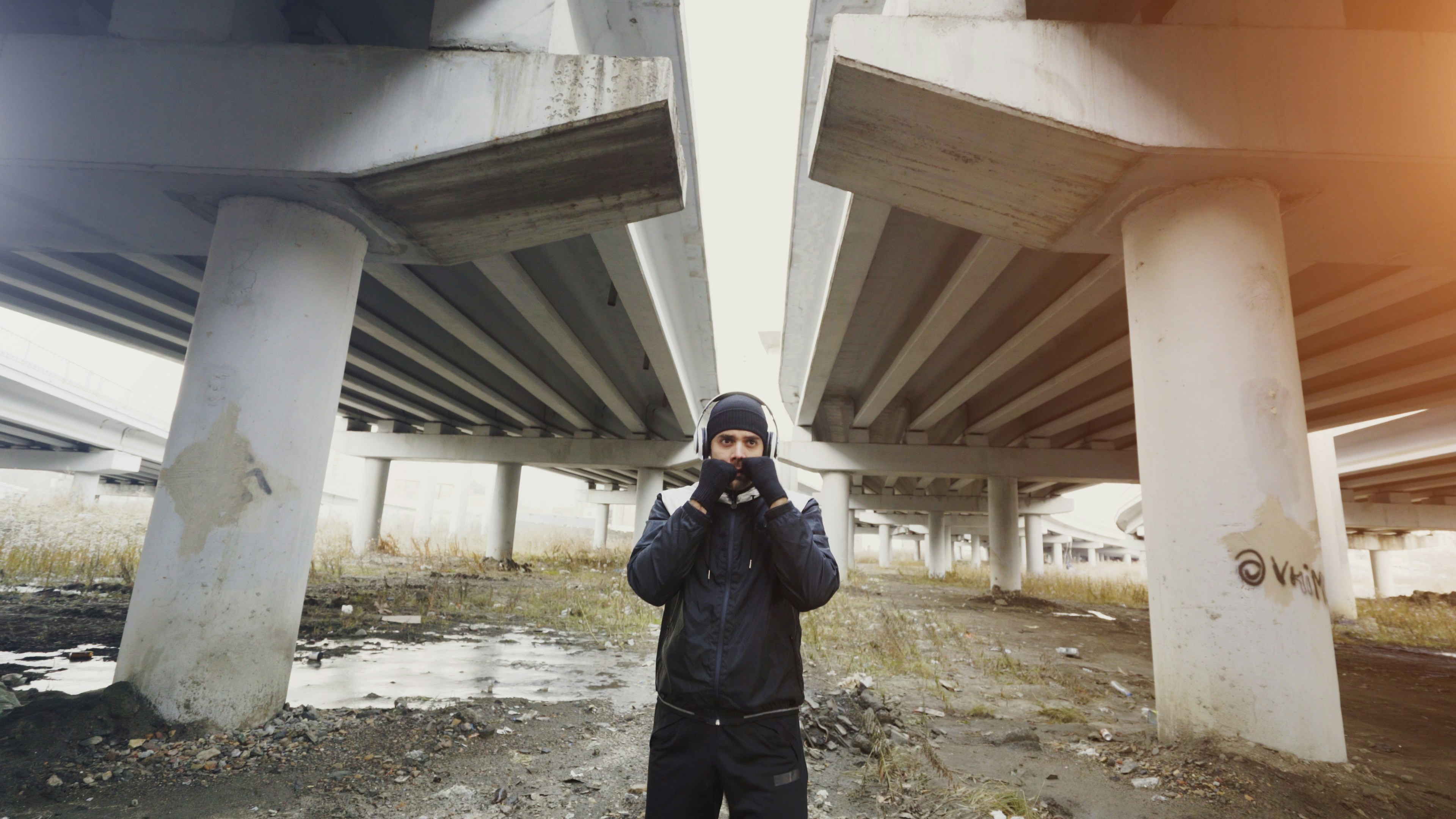 Man in dark clothing stands under concrete overpasses
