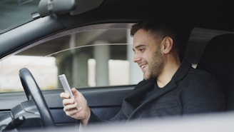 Man smiling while looking at his phone in car