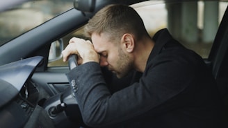 Man resting head on steering wheel in car.