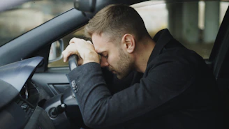 Man resting head on steering wheel in car.