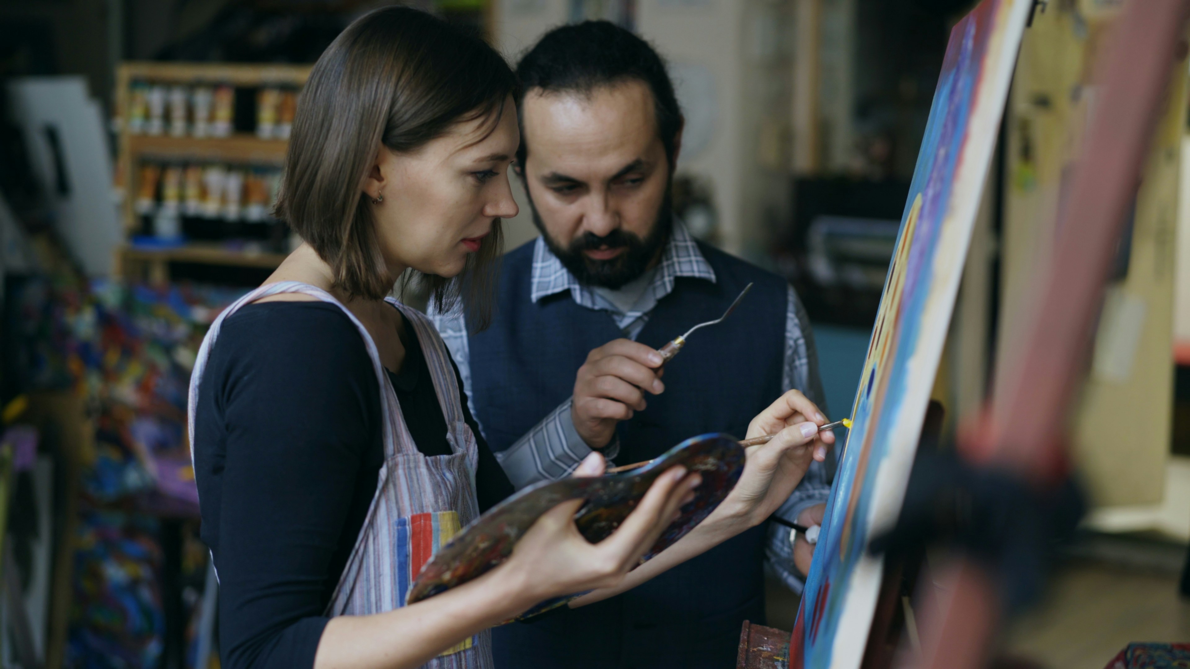 Two artists painting on a canvas together.