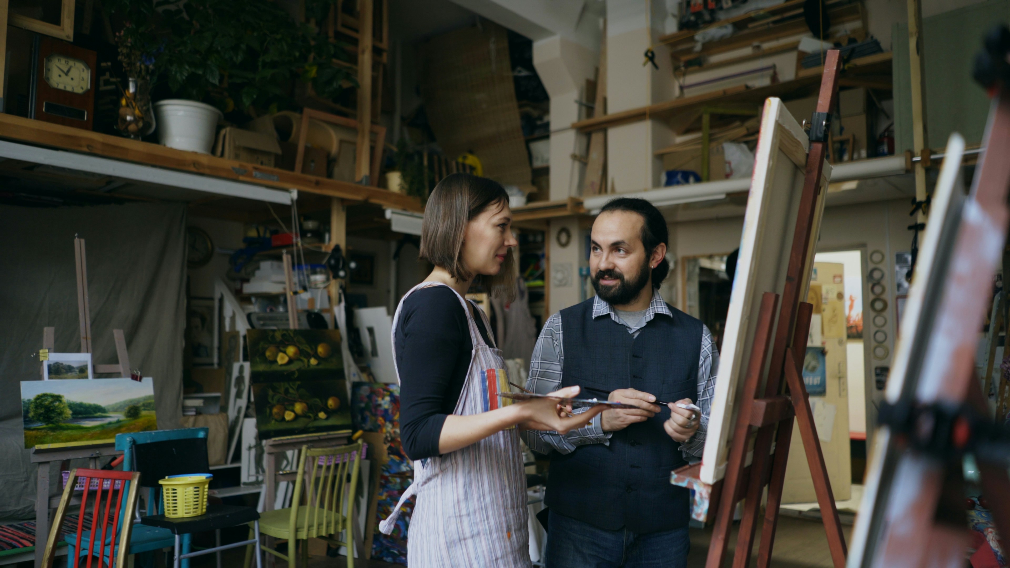 Smiling artist man teaching young woman to draw paintings and explaining the basics in art studio