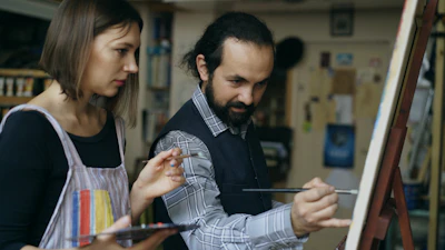 Artist teaching student painting on easel in studio