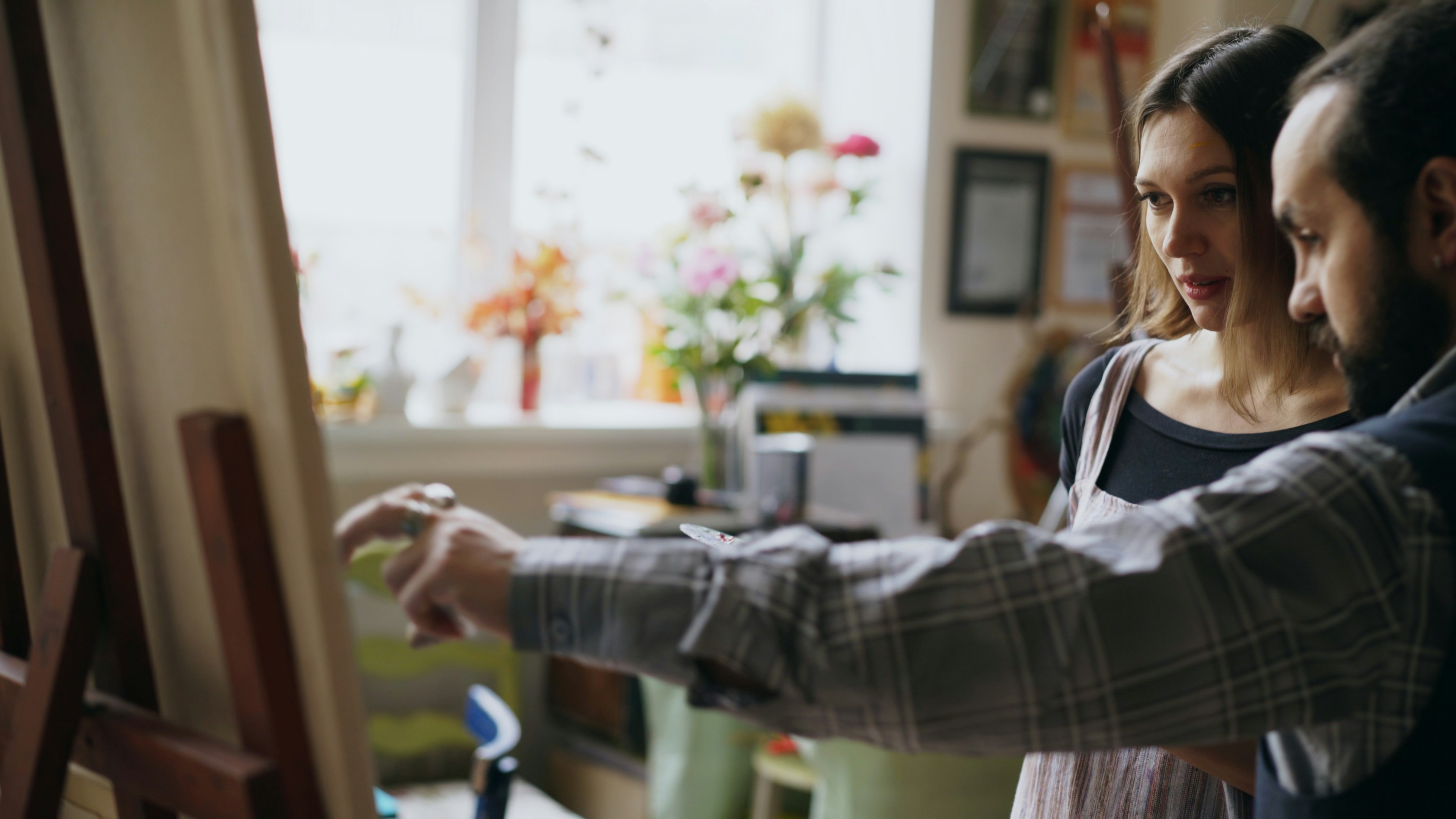 Skilled artist man teaching young girl painting on easel at art school studio