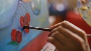 Hand painting red flowers on a blue canvas.