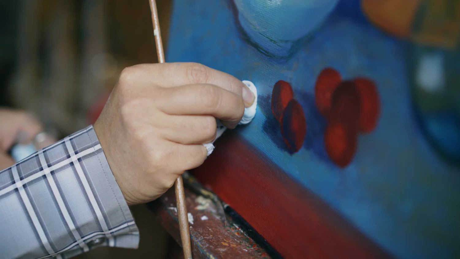 A gloved hand rolling a cotton swab across the surface of a painting