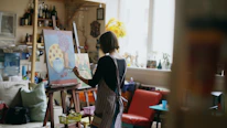 Artist painting on canvas in a sunlit studio.