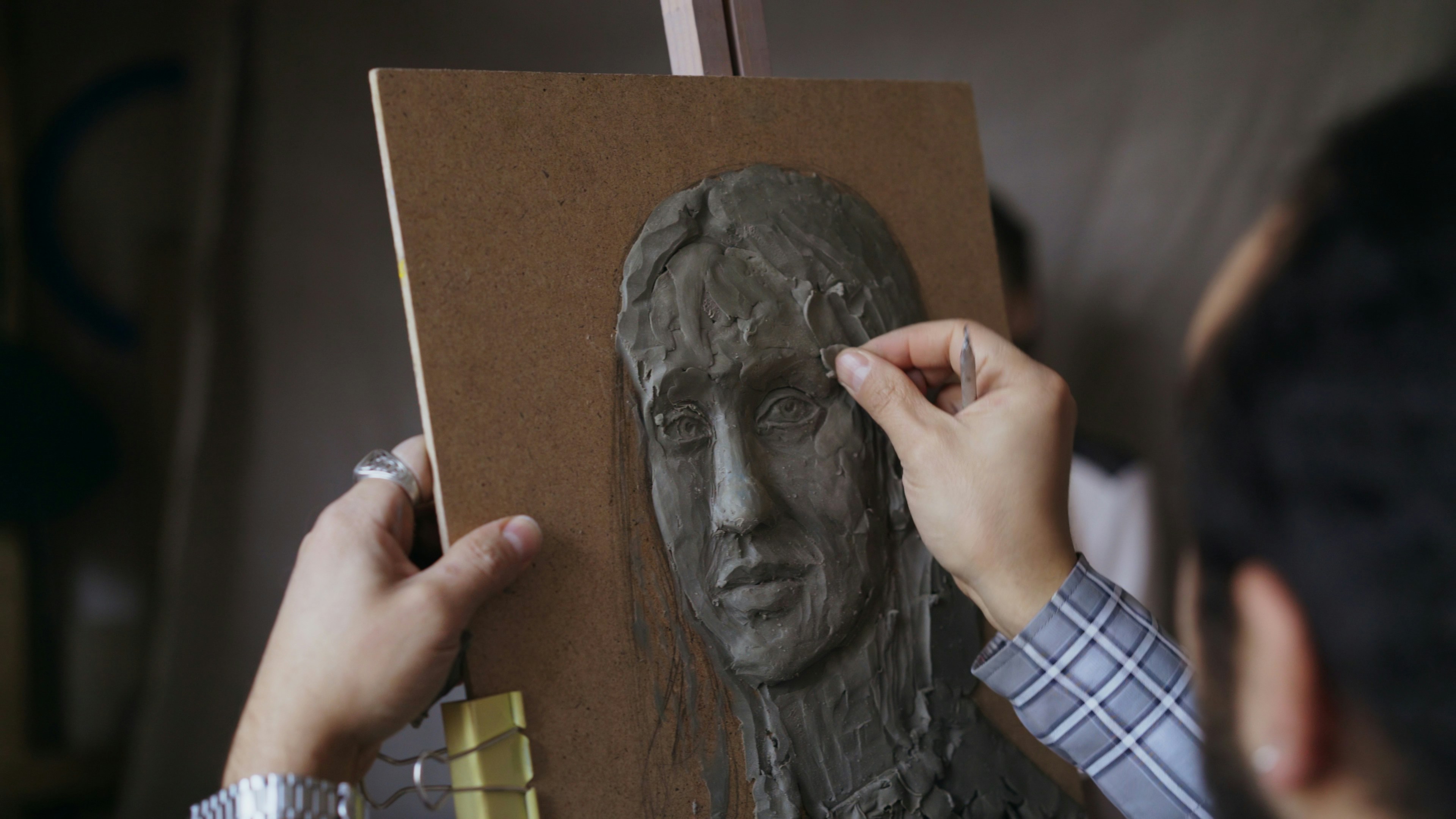Artist sculpting a clay portrait on a wooden board