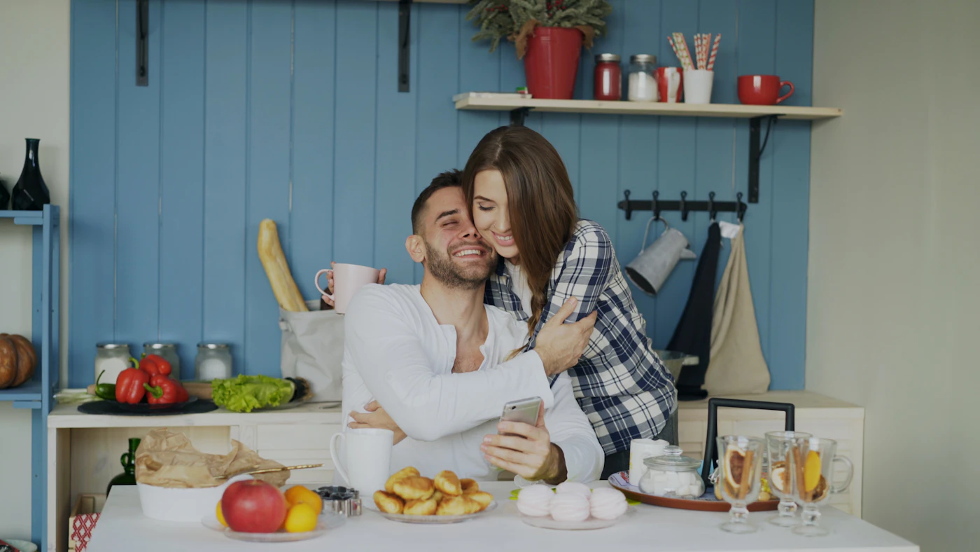 A couple smiling and embracing in their kitchen on a quiet morning
