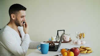 Man talking on phone while working on laptop at table.