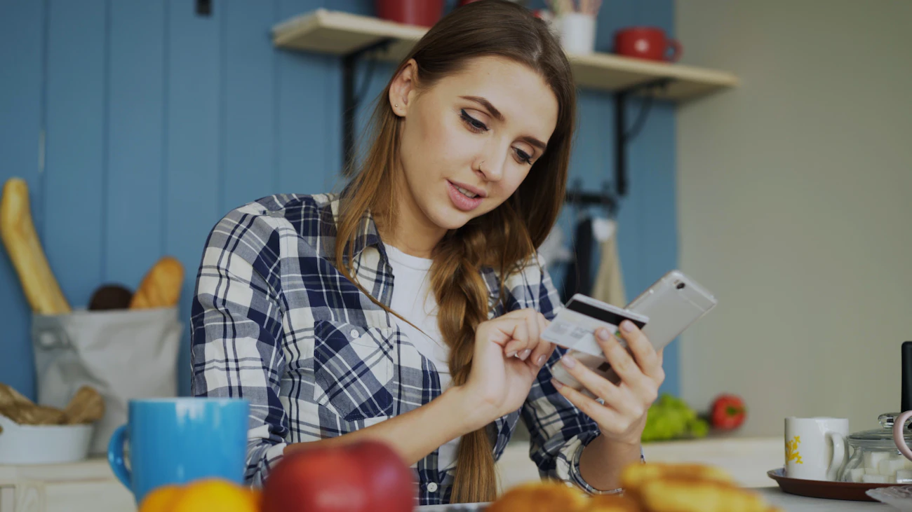 キッチンのテーブルでカードとスマートフォンを確認する女性