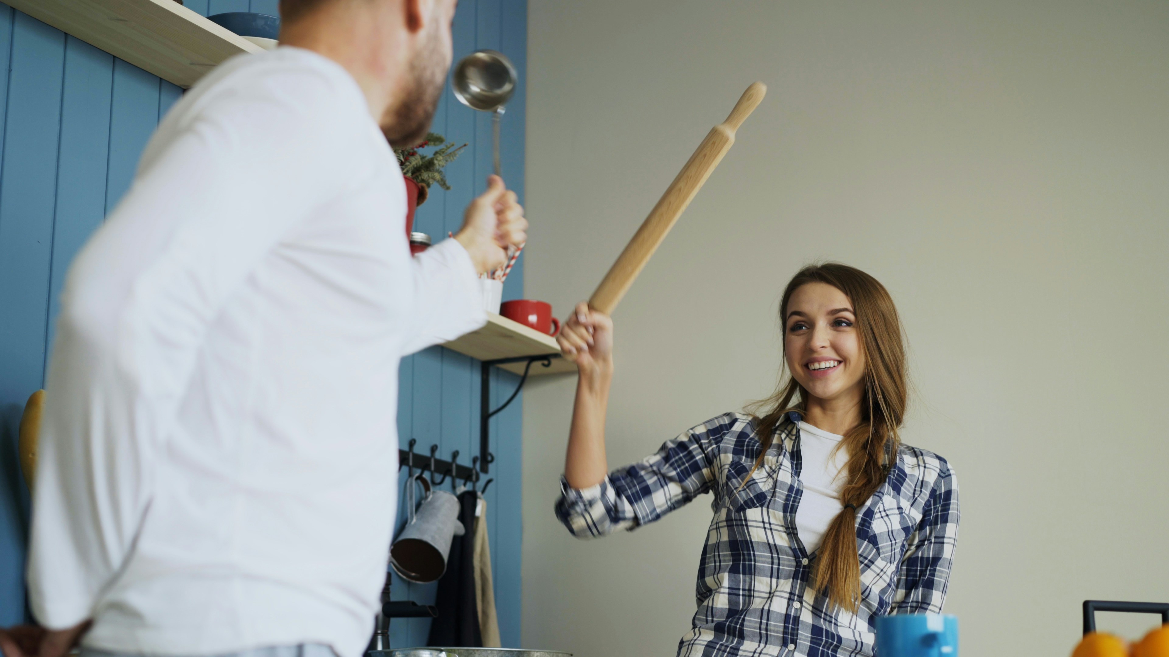 Couple playfully fighting with rolling pin in kitchen