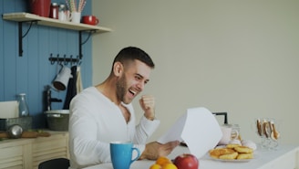 Man celebrating while reading a document at kitchen table.