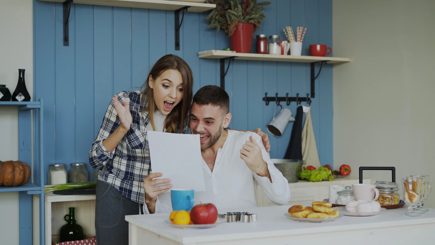Couple in their kitchen reading a letter together and smiling