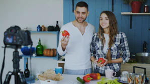 Couple holding red bell peppers in a kitchen.
