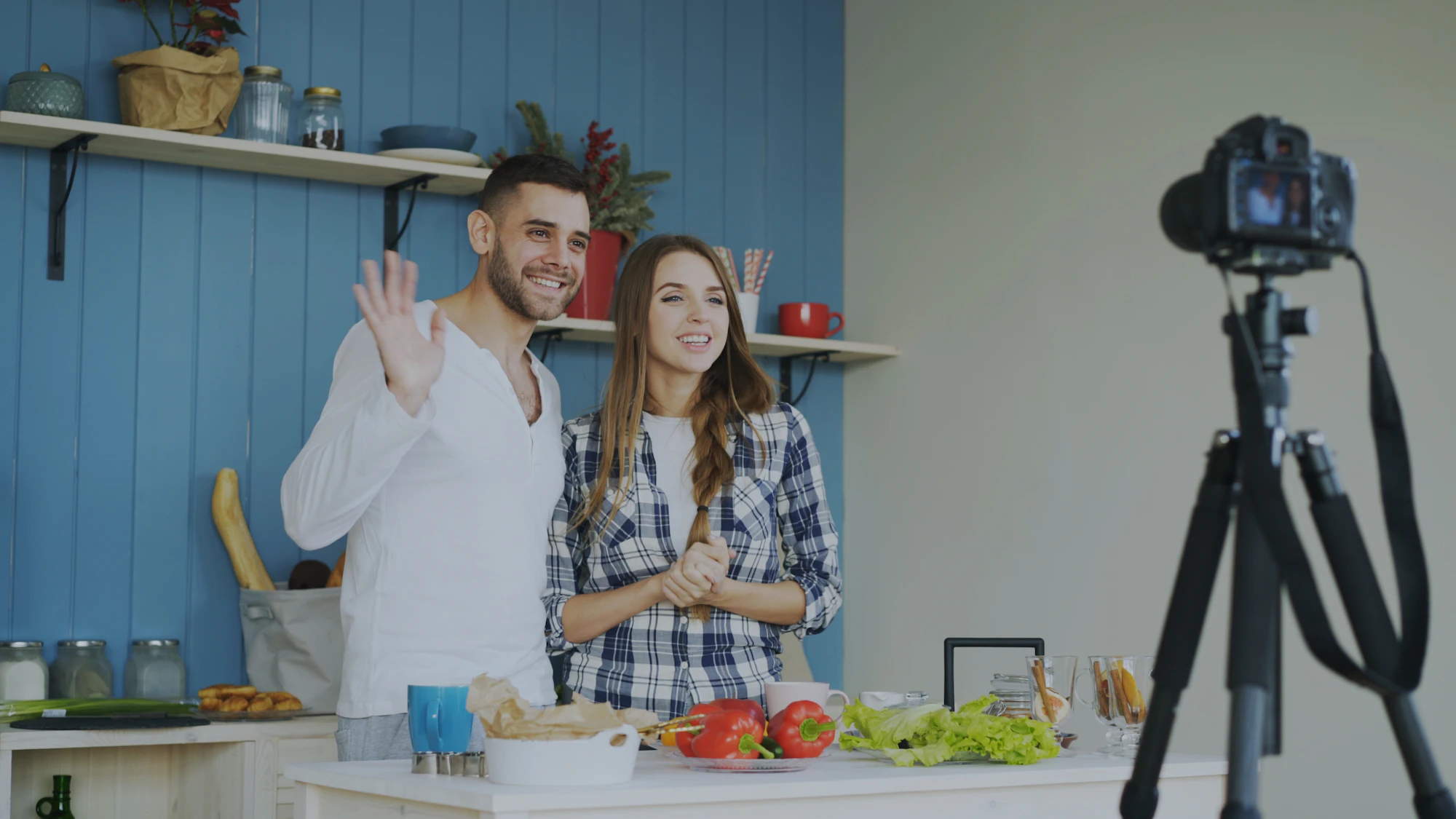 Two creators waving at the camera while filming in their kitchen