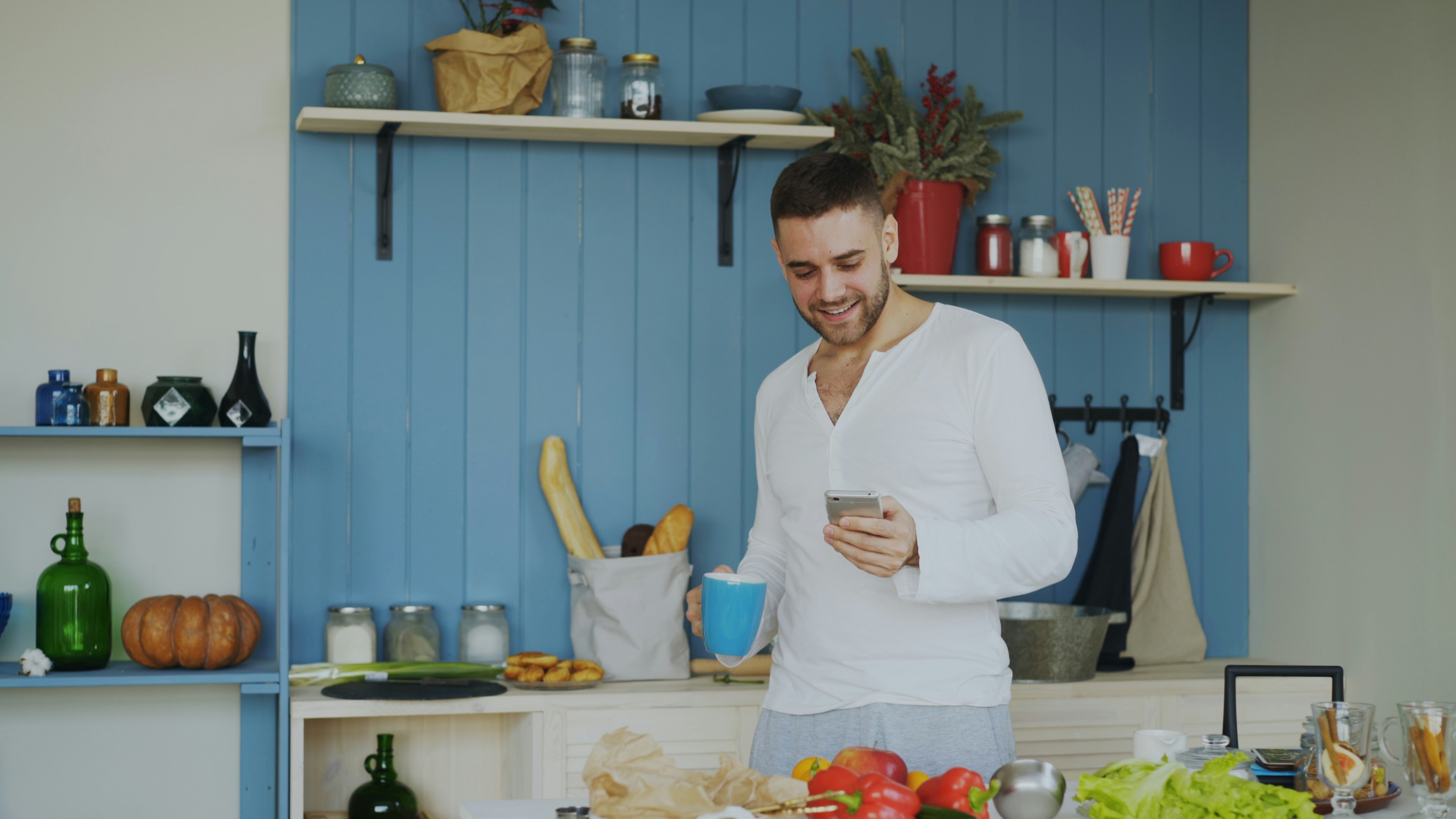 Man smiling while holding coffee and phone in kitchen