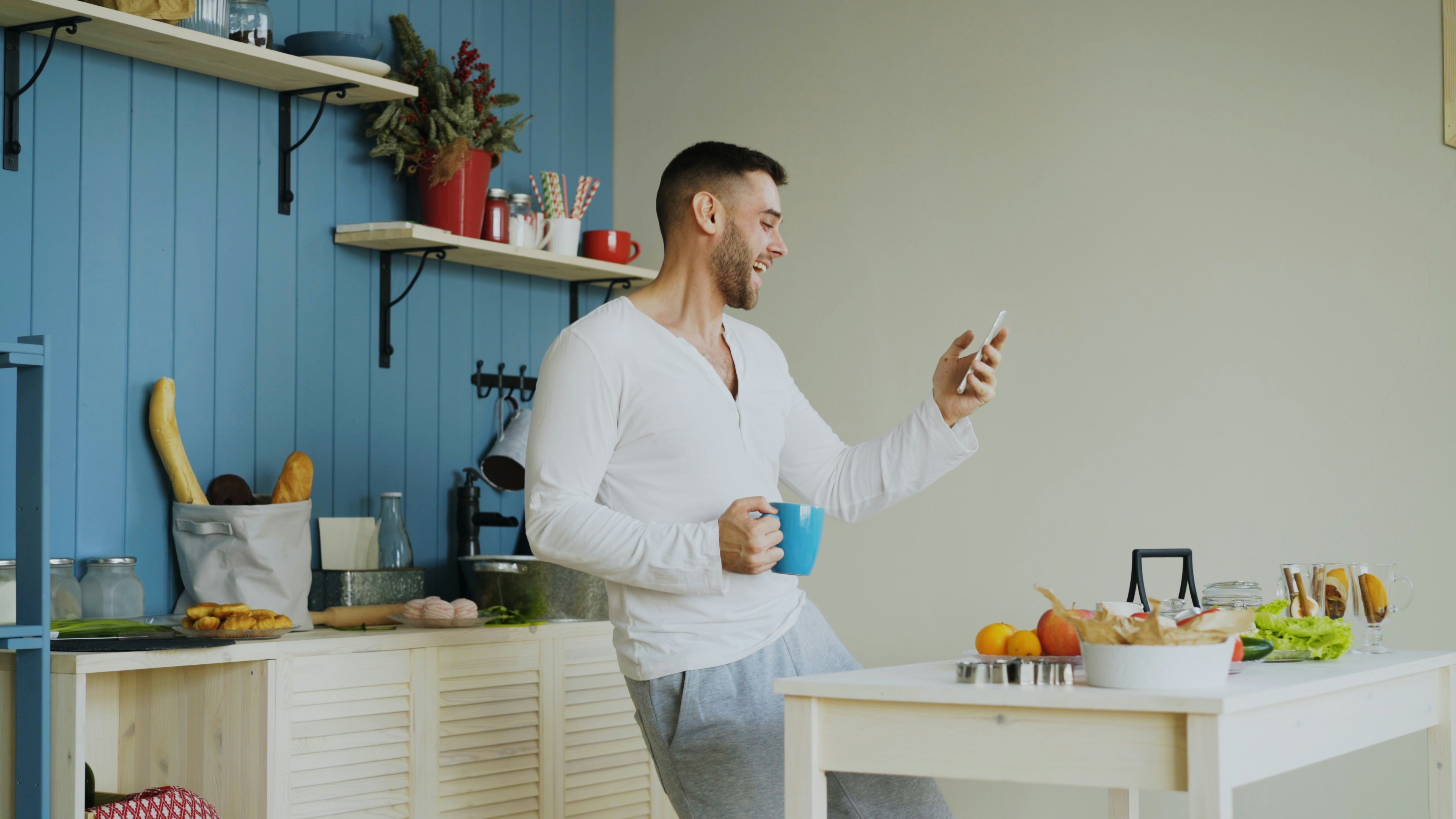 Man dancing in kitchen holding coffee and phone