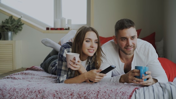 Couple relaxing on bed with coffee and remote.