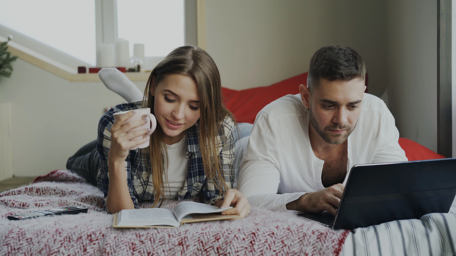 Couple relaxing together while reading and using a laptop, representing healthy independence and comfortable alone time within a relationship
