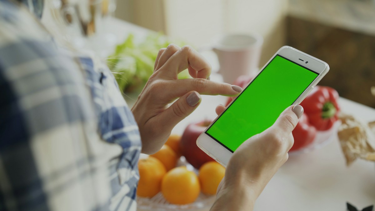 Person holding a smartphone with a green screen, ideal for displaying a Super Bowl potluck sign-up sheet template.