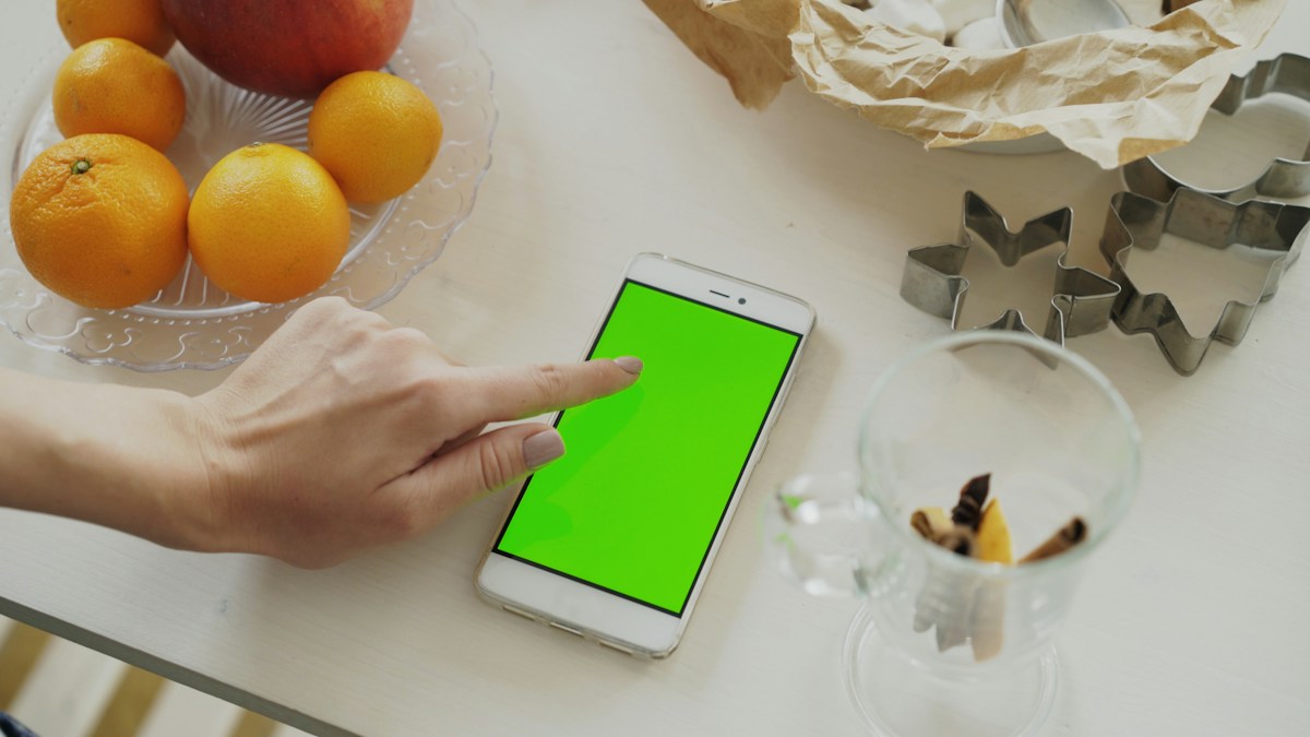 Hand using a smartphone with a green screen, illustrating online sign-ups for school payment collection.