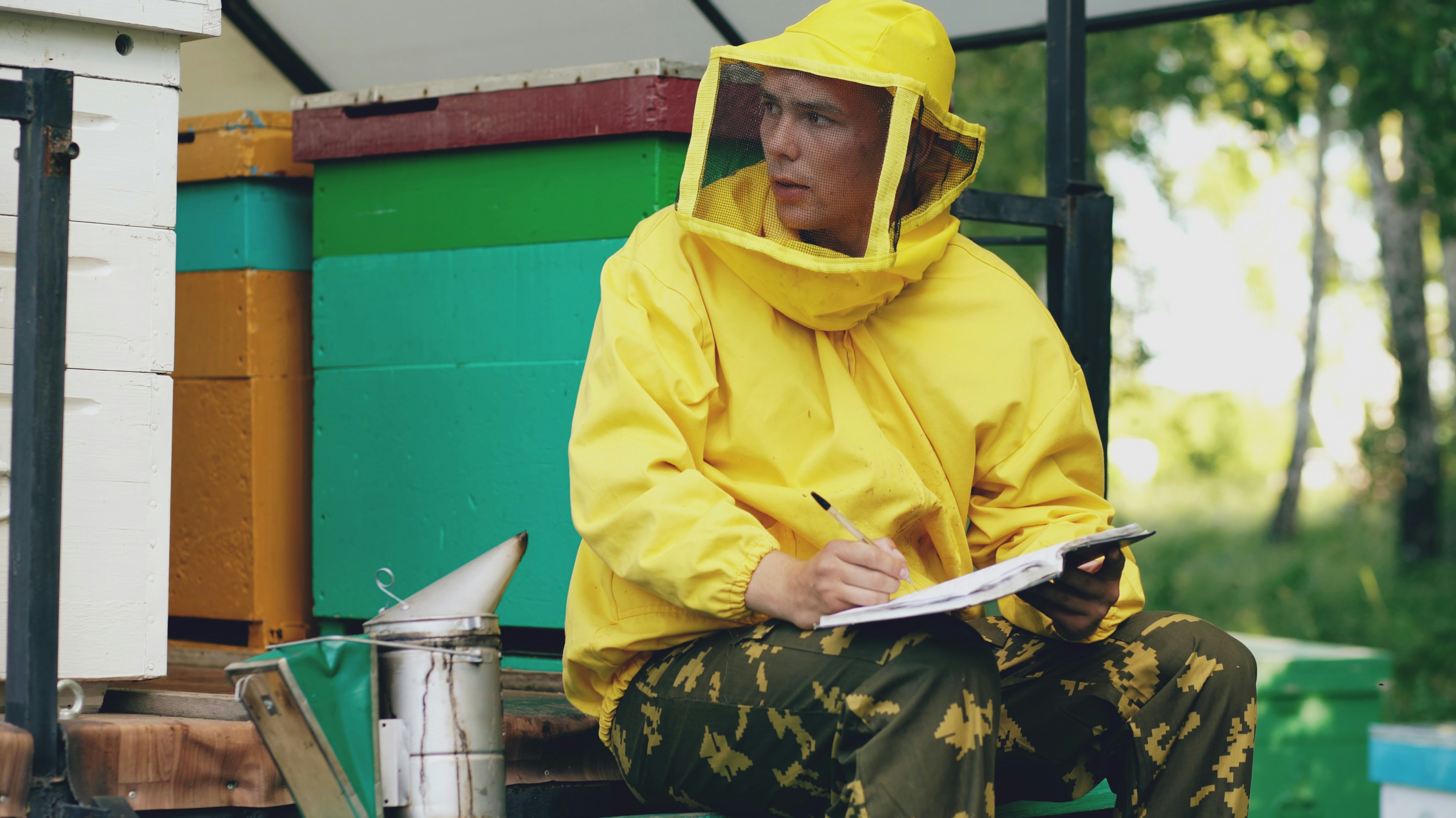 Beekeeper in protective suit writing notes near hives
