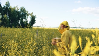 Beekeeper in yellow suit holding hive in field.
