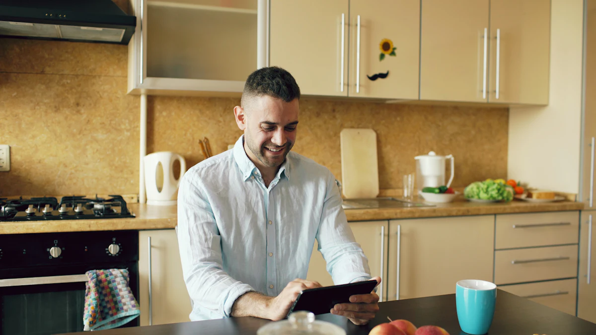 A young man smiling while checking his options on a tablet in his kitchen