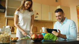 Couple preparing food and using tablet in kitchen.